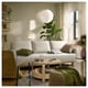 Warm living room: beige sofa-bed, wooden coffee table with glass, large plant, hanging white lamp, tower shelf, cosy decor, natural light.