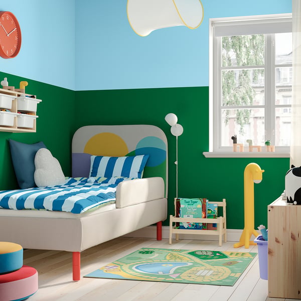 Kids room: green walls, blue-striped bed, colourful decor, giraffe lamp, wooden dresser.