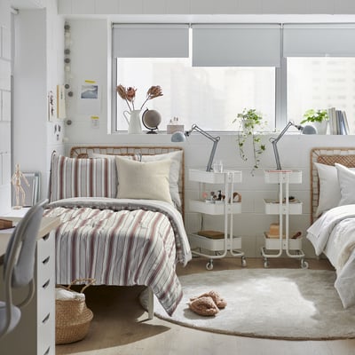Cosy bedroom with two GULDAKLEJA striped beds, bedside table with lamps, and natural light from windows.