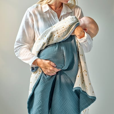 A person holding a sleeping baby wrapped in a soft, thick, blue and white dot blanket.