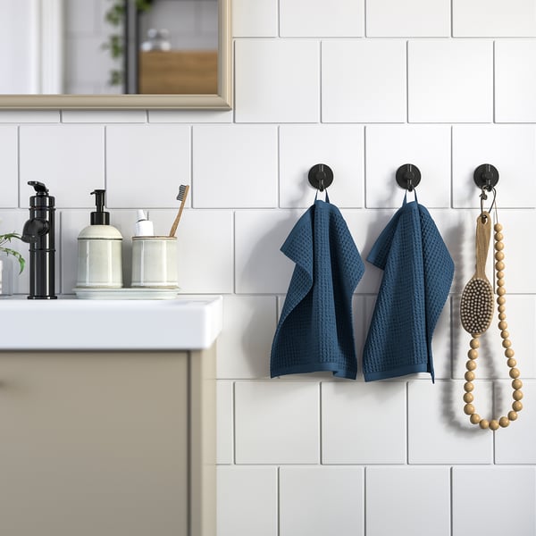 Bathroom with white tiles, two blue towels, black hooks, sink, and wooden toothbrushes.