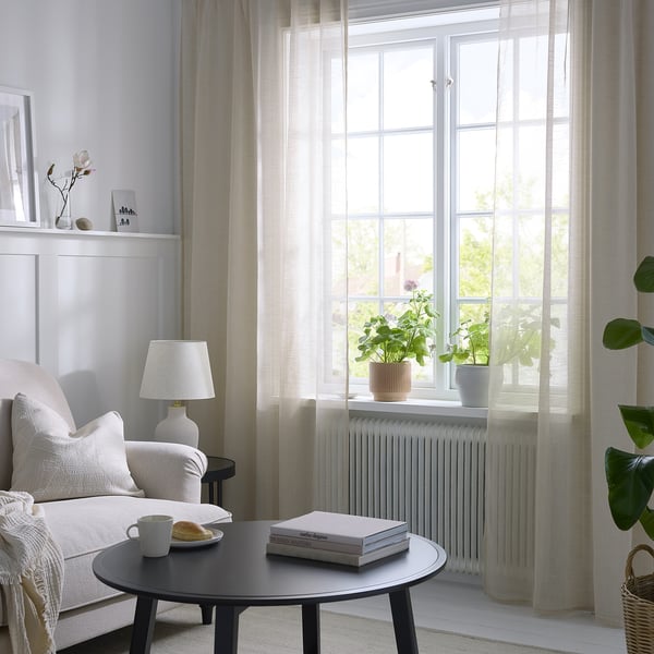Living room with HÄLLEBRÄCKA curtains, white couch, black table, lamp, plants. Airy feel.