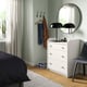 Bedroom with white HAUGA chest, round mirror, black lamp, and blue chair.