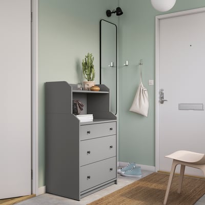 Minimalist entryway with grey HAUGA chest, mirror, green wall, white door, light wood stool, potted plant, and hanging bag.