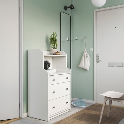 White HAUGA chest with 3 drawers, top shelf, next to door with hooks, small plant, and light.