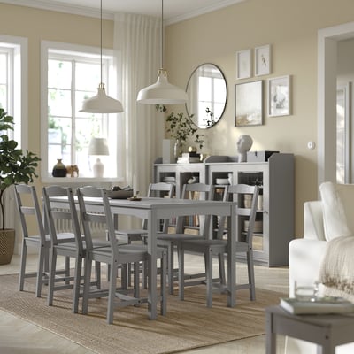 Modern dining area with grey wooden table, chair, rug, white accents, and large windows.