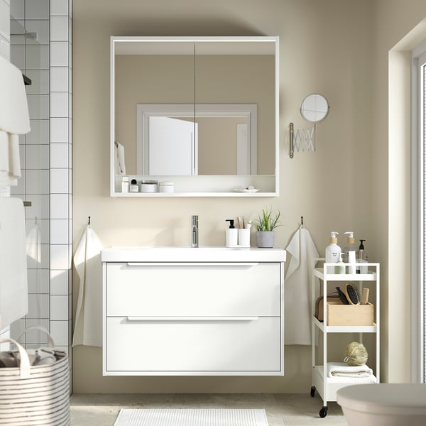 Modern white bathroom vanity with 2 drawers, mirror cabinet, small plant, toiletries.
