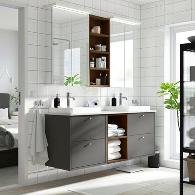Modern bathroom with dark grey double vanity, white sinks, plants, and mirror reflecting bedroom.