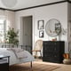 Cosy bedroom with dark brown HAVSTA dresser, mirror, chair, and plant.