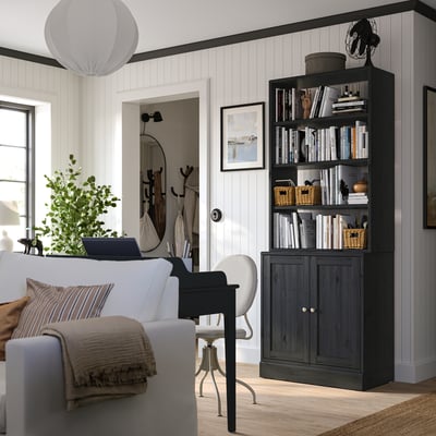 Cosy home office with white sofa, black desk, and dark wooden bookshelf filled with books and decorative items.