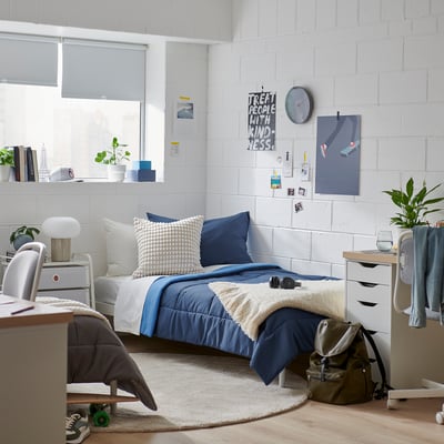 Cosy bedroom with HEDFRYLE blue comforter set; soft, recycled material. Bed centred, flanked by nightstands, under large window.