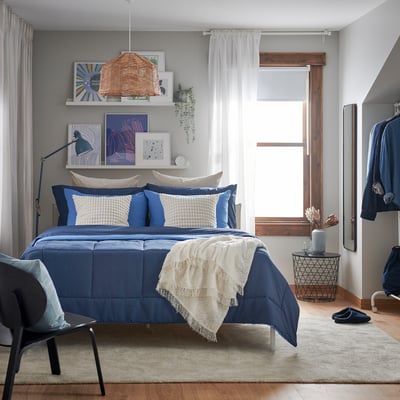 Bedroom with blue HEDFRYLE comforter on bed, white pillows, blue chairs, and decorations on wall.