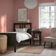 Cosy bedroom with red walls, black HEMNES bed frame, white linens, small bedside table with lamp, chair, and wicker basket. Window lets in light.