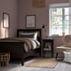HEMNES bed & bedside table in dark brown. Beige armchair, rug, & flower prints. Cosy, well-lit room.