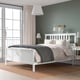 HEMNES white bed in bright room, grey linens, pendant lamp, large window with curtains, bedside table with gold lamp and books.