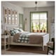 Bedroom with white HEMNES bed, green accents, green-potted plants, natural light, wooden floor, picture frames, lamps, dresser, and rug.