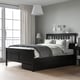 Modern bedroom with HEMNES black wooden bed, grey linens, white lamps, large window, and beige rug.