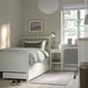 Minimalist bedroom with HEMNES bed, lyngör base, drawers, bedside table, chandelier, grey pillows, floral rug.