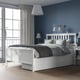 White HEMNES bed with 4 drawers, grey bedding, wall lamps, light grey curtains, bedside table with lamp.