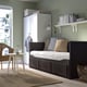 Modern bedroom with grey HEMNES day-bed, white bedding, brown pillows. Under wall shelf with books and clock, next to white wardrobe.