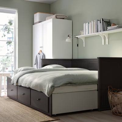 Bedroom with HEMNES day-bed, storage drawers, & tall cabinet. Window, wall lamp, & bookshelf visible.