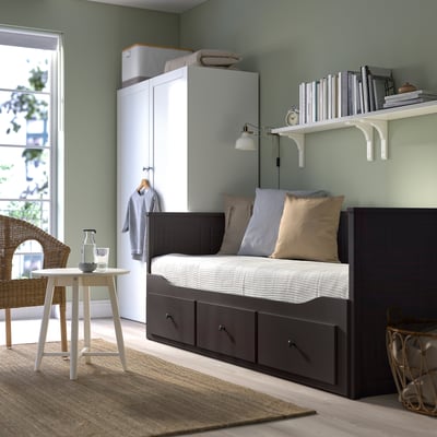 Modern bedroom with HEMNES day-bed, storage, bookshelf, wardrobe, and rattan chair with table holding carafe and glasses.