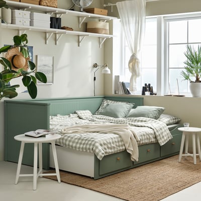 HEMNES grey-green day-bed/sofa with drawers, foam mattress, & chequered blanket in small, cosy room.