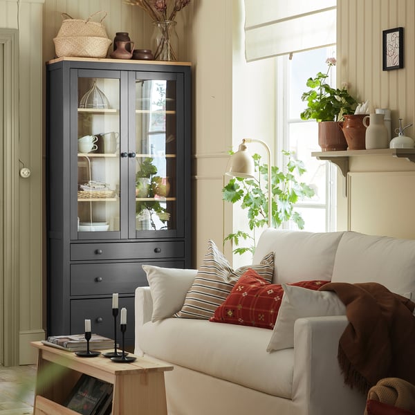 Dark grey HEMNES cabinet in cosy living room with red pillows and window.