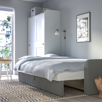 Tidy bedroom with light blue walls, white bed with grey underframe, wall lamp, and large window with seat.