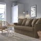 Cosy living room with brown sofa, pillows, side table, lamp, rug, wardrobe, wicker chair, and picture.