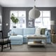 Modern living room with HYLTARP blue sectional sofa, light grey rug, white pendant lamp, wooden floor, and large window.