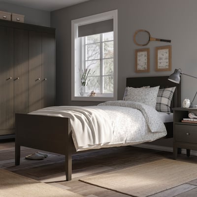 Modern bedroom with IDANÄS bed, black wood, white linens, grey walls, wooden floor, large window, lamp, frames, and closet.
