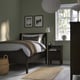 Bedroom with dark brown IDANÄS bed, green wall, large window, basket, bedside table with lamp and clock