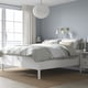 Modern white bed in blue room. Large, plush, high with white pillows. Large rug, gold sconce, patterned rug.