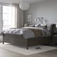 Modern, grey IDANÄS bed with drawers and a high mattress base, featuring clean lines and a streamlined design, positioned beside a large window.