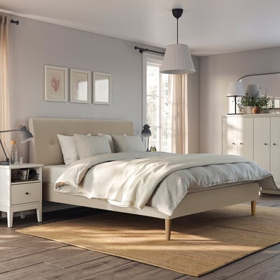 Minimalist bedroom with IDANÄS beige bed, decorative pillows, pendant lamp, rug, side lamp, wardrobe, and curtains.