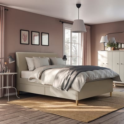 Modern bed with beige upholstery, sloping headboard, & soft-closing drawers. Large, fits well in room, light wooden floor.