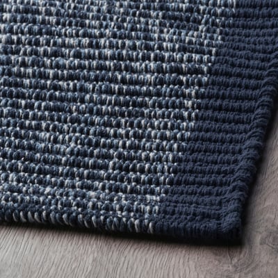 Dark blue door mat with white flecks, laid on wooden floor, textured surface, edge detail visible.