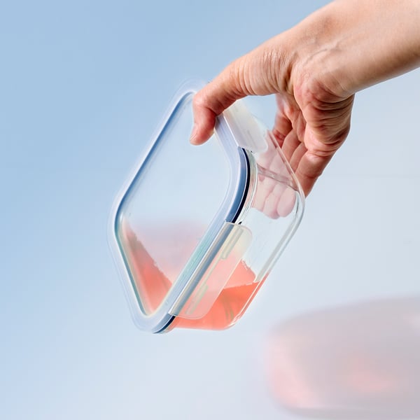 A hand holds a clear IKEA 365+ container with a leak-proof lid, showcasing its water-tight seal.