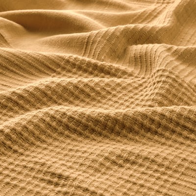 Close-up of a textured, golden-brown cotton bedspread, showing intricate weave patterns and soft, inviting fabric.