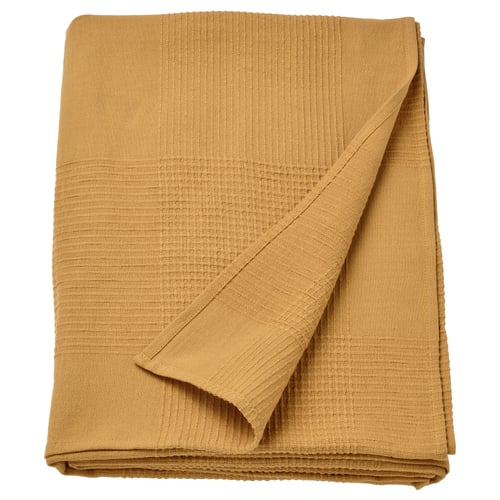 An a folded, mustard yellow cotton bedspread. Its rectangular with a textured, woven design, suitable for a single bed or as a large blanket.