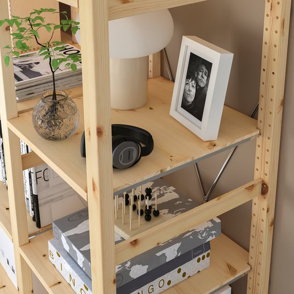 Wooden IVAR bookshelf holding photo frame, headphones, lamp, vase with plant, and game pieces.