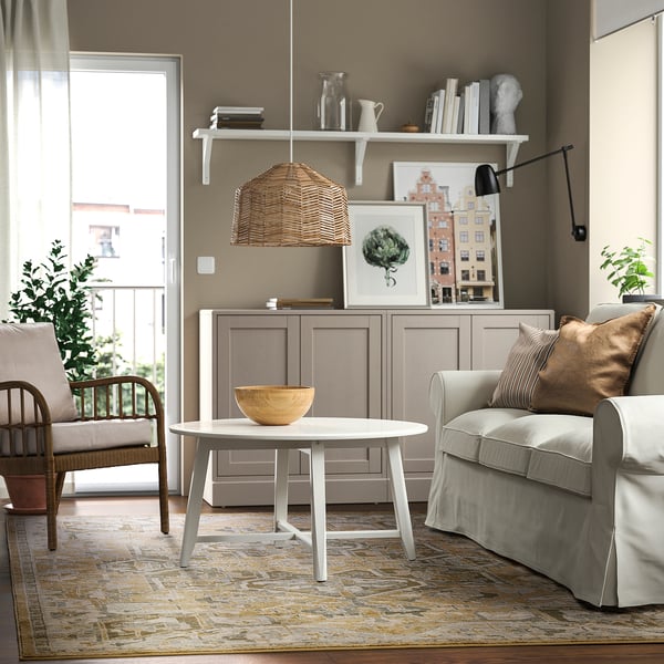 Modern living room with beige & grey rug, soft pastels, durable. Wooden table, grey cabinet, light grey sofa, wicker lamp.