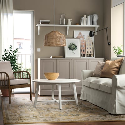 Modern living room with beige & grey rug, soft pastels, durable. Wooden table, grey cabinet, light grey sofa, wicker lamp.