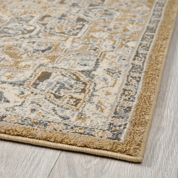 Elegant, beige area rug displayed on wooden floor. Intricate, neutral pattern and durable, stain-resistant material.