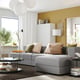 Modern living room with grey modular sofa, beige cushions, yellow wall, white lamp, and large window with curtain.