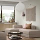 Contemporary living room with beige sectional, pendant light, wall hanging, abstract art, and wooden cabinet with vase.