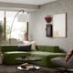 Modern living room with a green JÄTTEBO modular sofa, glass coffee table, large floor lamp, abstract wall art, and grey concrete walls.