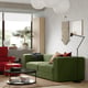 Modern living room with a green JÄTTEBO sofa, red armchair, coffee table, and large window with plant.