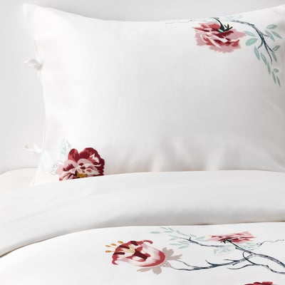 White bedding set with intricate floral designs in shades of red and green. Smooth, sateen-woven fabric made from soft lyocell material.